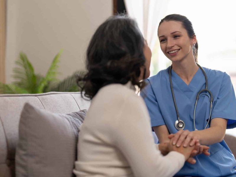 Happy patient is holding caregiver for a hand while spending time together. Elderly woman in nursing home and nurse.